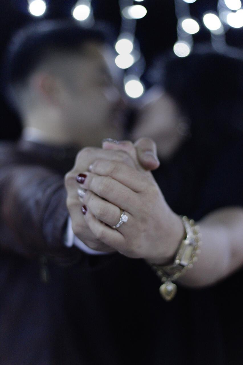 Close-up of a couples hands holding together, woman wearing an engagement ring and pearl bracelet, with holiday lights blurred in background
